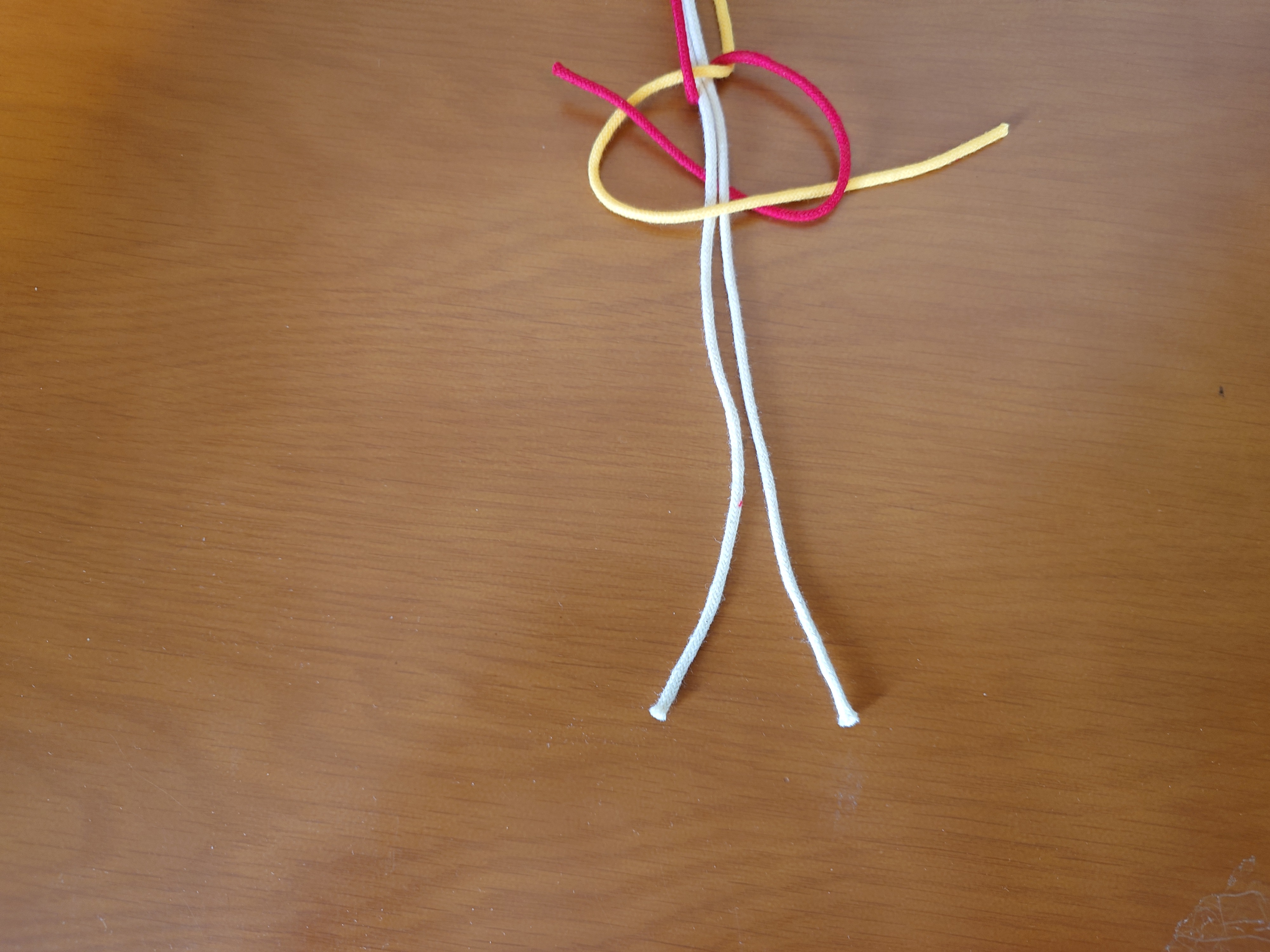 右端の紐を、その他の全ての紐の裏側から通して、三角の中から出す